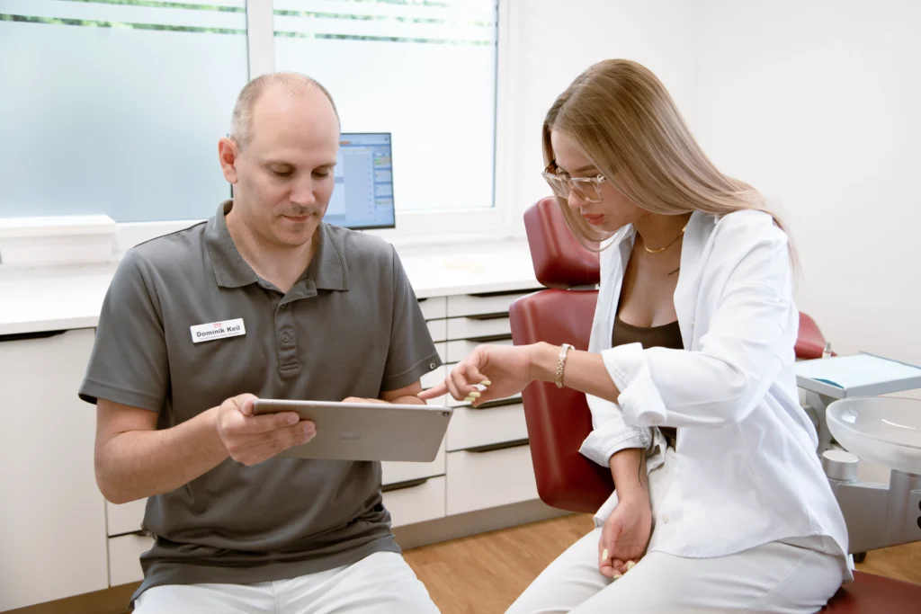 Fachzahnarzt Dominik Keil berät eine Patientin mit einem Tablet in der Kieferorthopädie Saarburg.