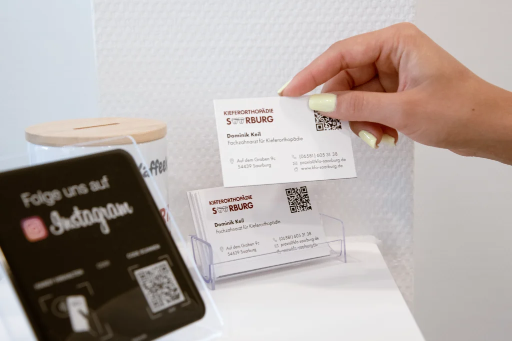 Patientin nimmt eine Visitenkarte der kieferorthopädischen Praxis KFO Saarburg aus einem Kartenhalter.