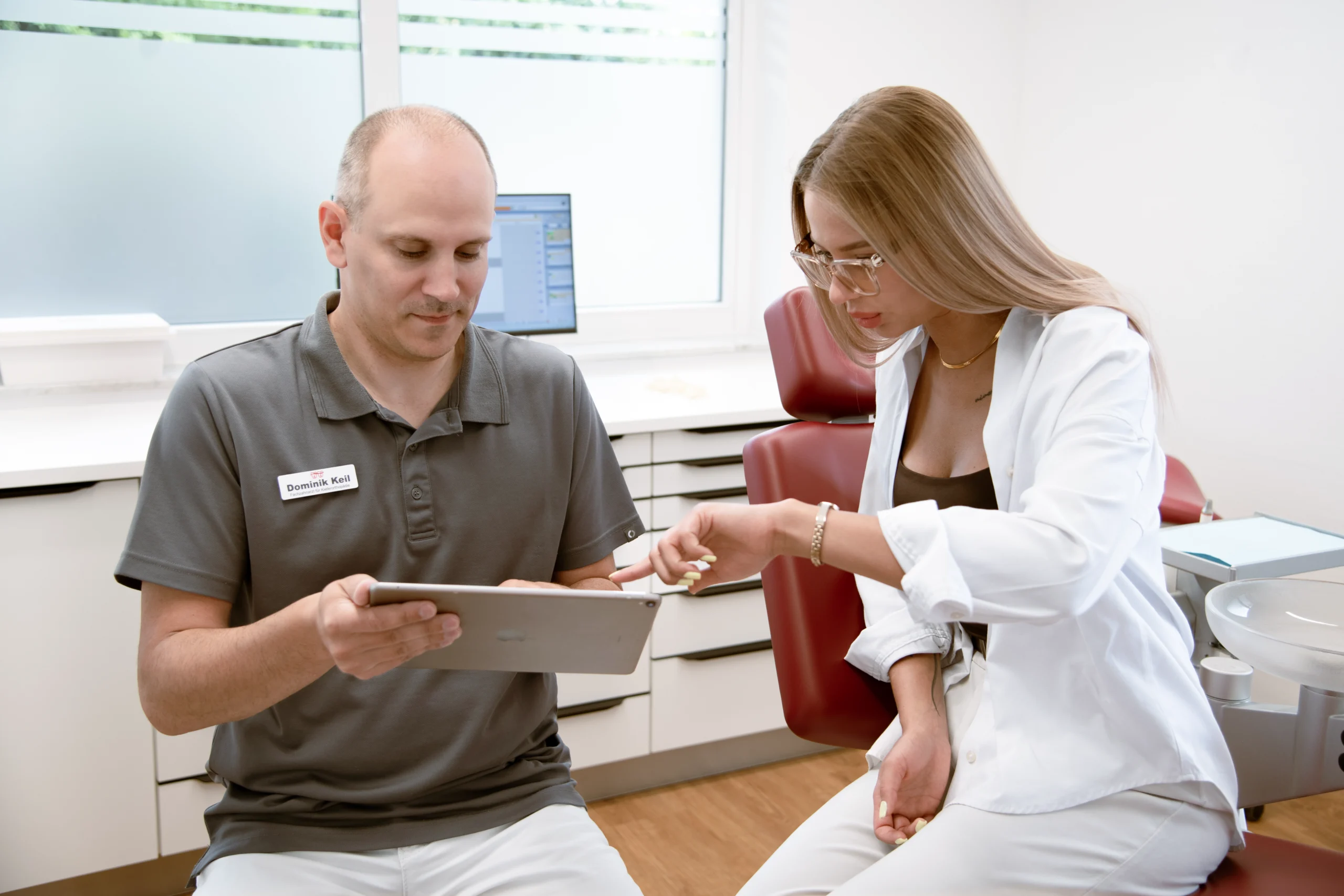 Kieferorthopäde Dominik Keil berät eine Patientin mit einem Tablet in der kieferorthopädischen Praxis.
