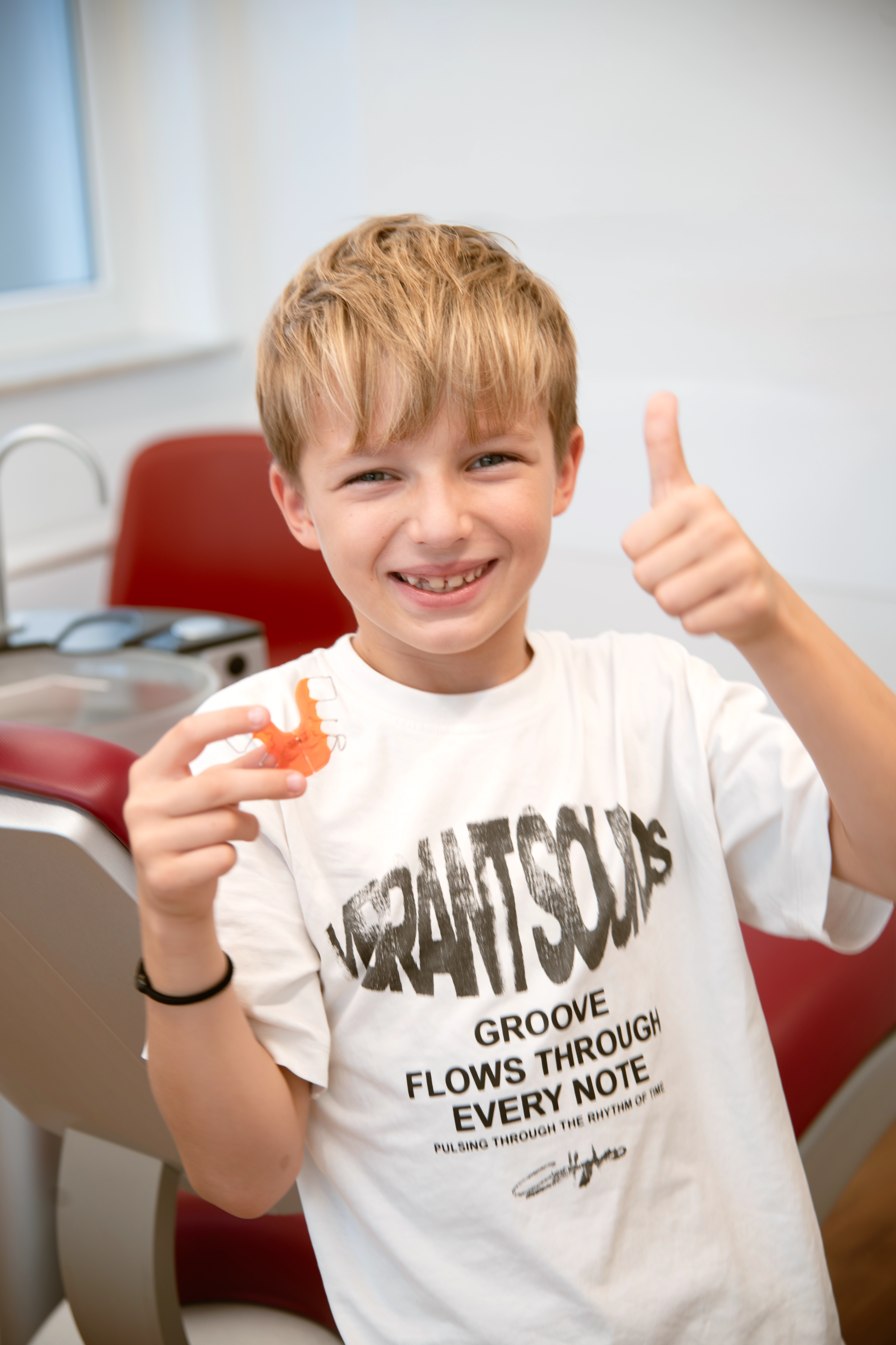 Zufriedenes Kind in der kieferorthopädischen Praxis mit herausnehmbarer Zahnspange in der Hand.
